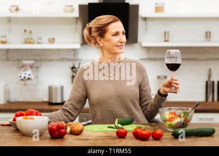 Pleasant beautiful lady spending time in kitchen and drinking wine Stock Photo
