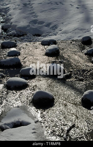 Sparkling water flow between stones covered with snow in early spring during thaw Stock Photo