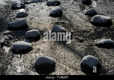 Sparkling water flow between stones covered with snow in early spring during thaw Stock Photo