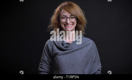 Closeup portrait of middle-aged extravagant redhead female in glasses being happy and smiling cheerfully while looking straight at camera Stock Photo