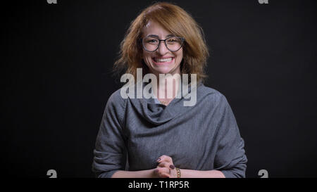 Closeup portrait of middle-aged pretty redhead female in glasses being excited and celebrating an accomplishment while looking straight at camera Stock Photo