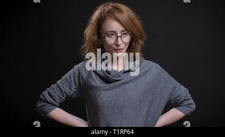 Closeup portrait of middle-aged extravagant redhead female in glasses being frustrated and having hands on the hips in front of the camera Stock Photo