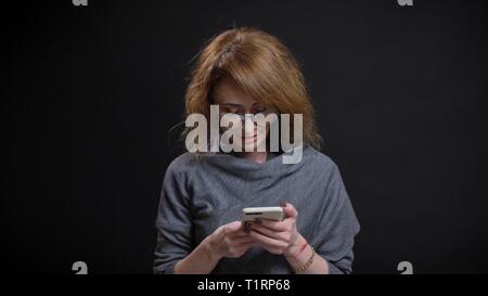 Closeup portrait of middle-aged extravagant redhead female in glasses texting on the phone in front of the camera Stock Photo