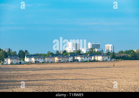 View over a harvested field and small houses to the satellite city Gropiusstadt in Berlin-Neukoelln illuminated by the sun. Stock Photo