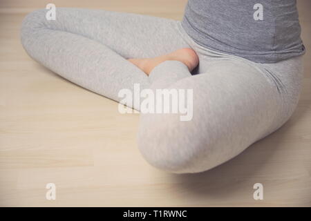 Teen Girl in Turkish Sitting Position in Grey Leggings on Wooden Floor Closeup Stock Photo