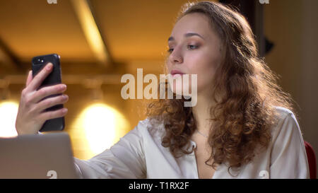 Portrait of concentrated young businesswoman making selfie-photos using smartphone on office background. Stock Photo