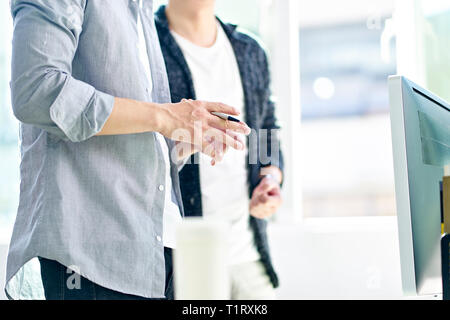 asian corporate executives standing in front of computer discussing business plans in modern office. Stock Photo
