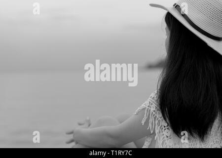 Pensive lonely young Asian woman. Side view of woman with sad feeling in black and white scene sit by the sea. Depressed and stressed girl looking to  Stock Photo