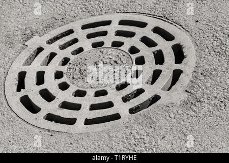 Dirty round sewer manhole cover installed in gray street pavement Stock Photo