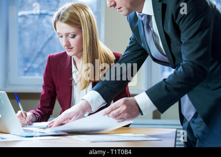 Business partners discussing documents and ideas at meeting. Man and woman in suits working with papers around table in the office. Workspace Stock Photo