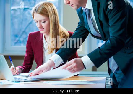 Business partners discussing documents and ideas at meeting. Man and woman in suits working with papers around table in the office. Workspace Stock Photo
