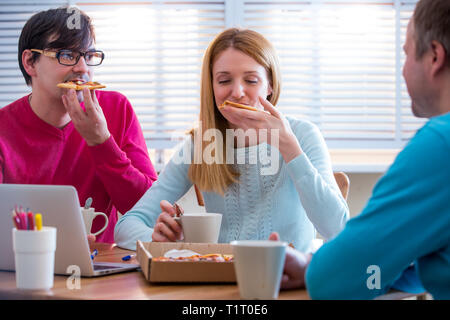 Happy business People Having Meeting And Eating Pizza in office.  Three young cheerful colleagues having lunch together at work. Creative team around Stock Photo