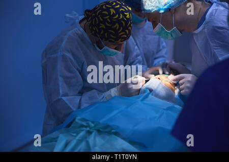 Surgical team performing surgery in modern operation theater,Team of doctors concentrating on a patient during a surgery,Team of doctors working Stock Photo