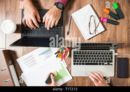 Two business persons working at office desk, typing and using laptop, top view, flat lay. Smart watch on hand and smart phone on the table. Coffee cup Stock Photo