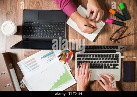 Two business persons working at office desk, typing and using laptop, top view, flat lay. Smart watch on hand and smart phone on the table. Coffee cup Stock Photo