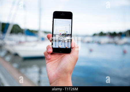 Hand taking a photo with smart phone. Picture of harbor with sailboats, seaside. Close-up Stock Photo