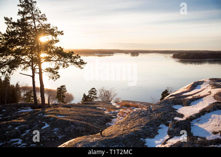 Finland, Helsinki, late autumn. Baltic sea, bay. Still water of the gulf, islands with forests. Low winter sun, dusk, pine trees on rock. Stock Photo