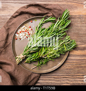 Seasoning a bunch of fresh fragrant rosemary on a brown wooden background. Square frame View from above. Stock Photo