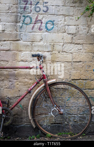 An old, rusting, abandoned red vintage bicycle in a Glasgow side street with graffiti on the wall behind it, Scotland Stock Photo