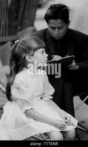 Street artist and little girl, Montmartre, 1968 - girl in party dress sits for a profile in the market below Sacré Coeur on a Sunday walk with her fam Stock Photo