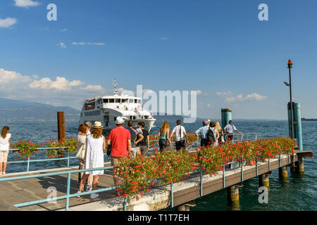 GARDONE RIVIERA, ITALY - SEPTEMBER 2018: People waiting on the ferry landing stage in Gardone Riviera on Lake Garda. In the background is a ferry Stock Photo