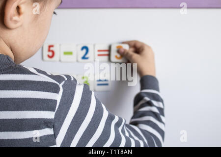 A child solves examples on a blackboard. The boy solves mathematical examples. The concept of education and school life. Stock Photo