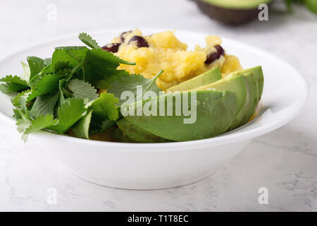 Healthy vegan brunch bowl with  grits, black beans,  avocado, topped fresh cilantro, Mexican style dish, close up, selective focus Stock Photo