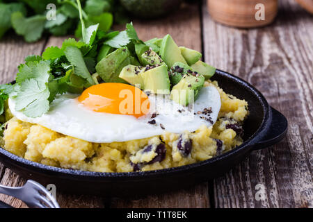 Healthy vegetarian  brunch with  grits, black beans,  avocado, topped with fried egg, fresh cilantro, Mexican style dish, close up, selective focus Stock Photo