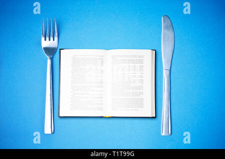 fork and knife with a book between, concept for reading is food for the brain Stock Photo