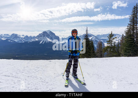 Young skier standing at the edge of a mountain range in sunny Lake Louise at the Canadian Rockies of Alberta, Canada. Stock Photo