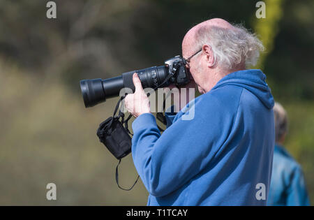 Senior man taking photographs with a DSLR and long telephoto lens. Side view of male taking photos with a digital camera. Pensioner hobby. Stock Photo