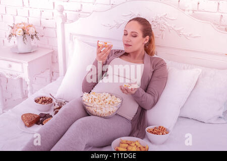 Fair-haired good-looking pregnant woman in comfortable clothes eating cornflakes Stock Photo