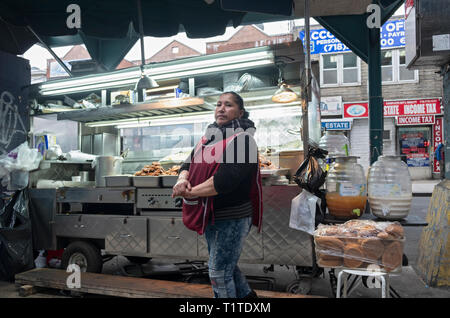A South American woman selling grilled meats & other foods from a cart just off Roosevelt Ave. and a few feet from the elevated subway trains . NYC Stock Photo