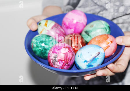 A child in his hands holding a plate with Easter eggs. Painted Easter eggs. Marble colored eggs. Pastel shades. Stock Photo