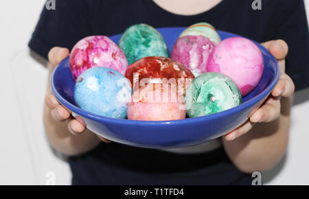 A child in his hands holding a plate with Easter eggs. Painted Easter eggs. Marble colored eggs. Pastel shades. Stock Photo