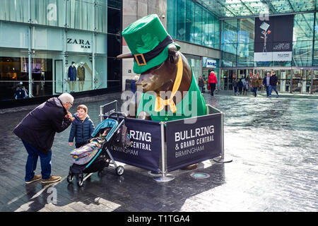 A small boy appears reluctant to have his photograph taken in front of the Bull Ring statue in Birmingham specially dressed in green for St Patricks’  Stock Photo