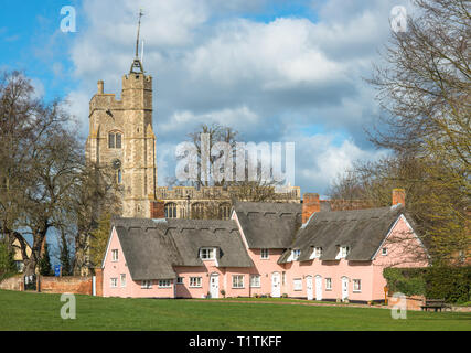 Thatched cottage painted in Suffolk pink with St. Mary the Virgin's Church on the village green. Cavendish, Suffolk, East Anglia, UK. Stock Photo