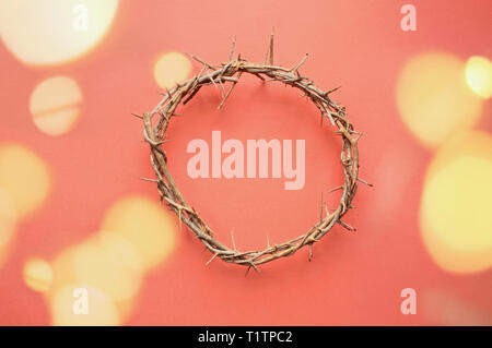 Crown of thorns like Jesus Christ wore with drops of blood on tips of thorns with bokeh lights over coral background. Perfect for Easter. Stock Photo