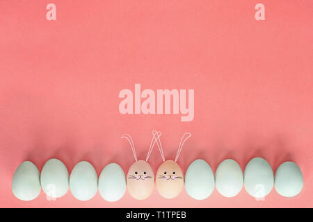 Decorated Easter eggs with cute bunny face and ears drawn on over a pastel background with room for copy space. Image shot from top view. Stock Photo