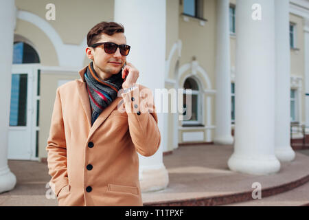 Young stylish businessman using smartphone in city. Handsome guy wearing classic clothes and accessories. Street fashion Stock Photo