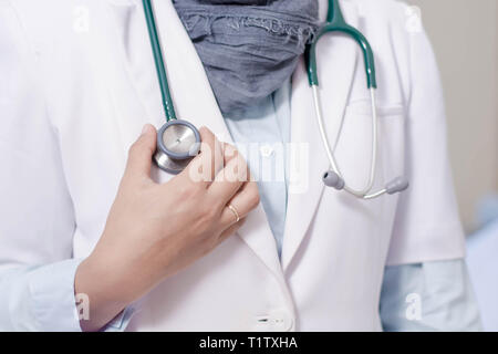 Front view body part of hijab female doctor hand holding stetoschope inside a hospital bed room Stock Photo