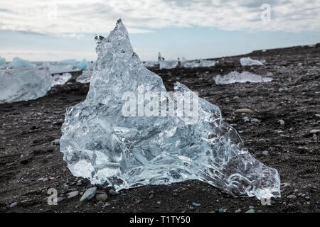 Isolated iceberg melting on black sand beach near Jokulsarlon glacial lagoon, a popular travel dastination and one of the natural wonders of Iceland,  Stock Photo