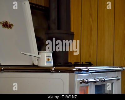 Economical wood-burning stove for cooking, baking and heating. White wood-burning stove in a kitchen of a home with a Turkish coffee pot on the fire. Stock Photo