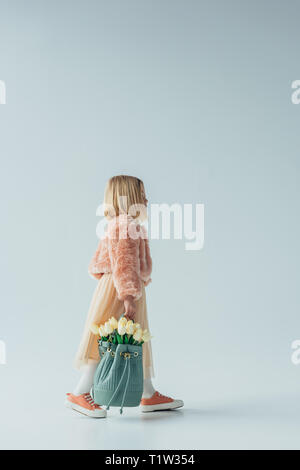 side view of cute kid holding bag with white tulips on grey background Stock Photo
