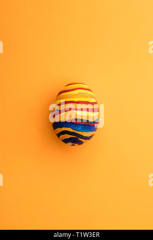 Detail of painted yellow Easter egg with red and blue stripes in orange background. Stock Photo