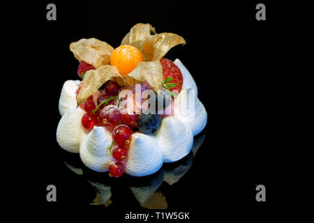 Close up of meringue cake with berries isolated on darkbackground. Stock Photo