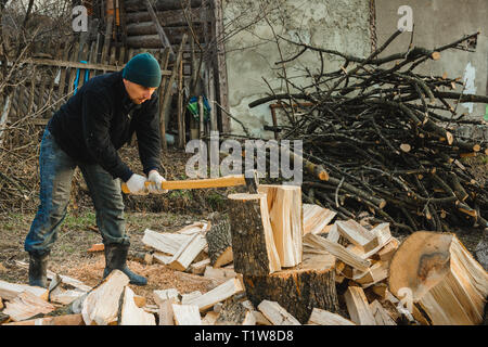 A strong man harvests firewood for the winter in the back yard of the house cutting the big and sturdy grass tree 2019 Stock Photo