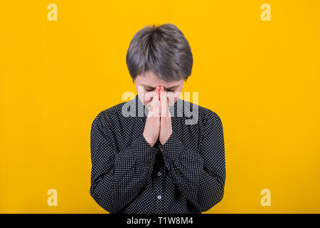 Concept of meditation and prayer. Young female standing in meditative pose against yellow wall, with closed eyes and calm face full of sense of inner  Stock Photo