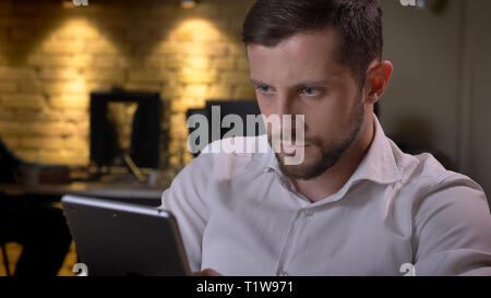 Closeup shoot of adult caucasian businessman texting on the tablet on the workplace indoors in the office Stock Photo