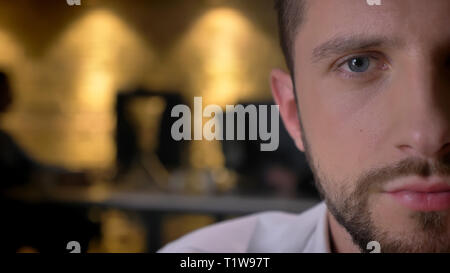 Closeup half-face front shoot of adult caucasian bearded male face with eyes looking at camera indoors with interior on the background Stock Photo